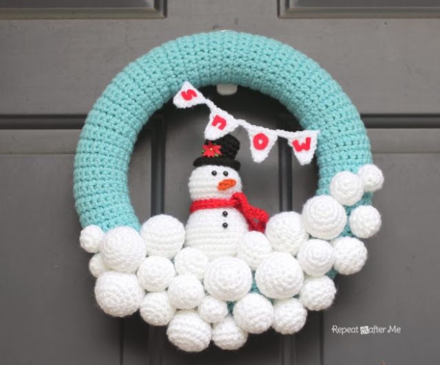 Crocheted wreath with a snowman sitting on top of snowballs and a blue arc covering the two.