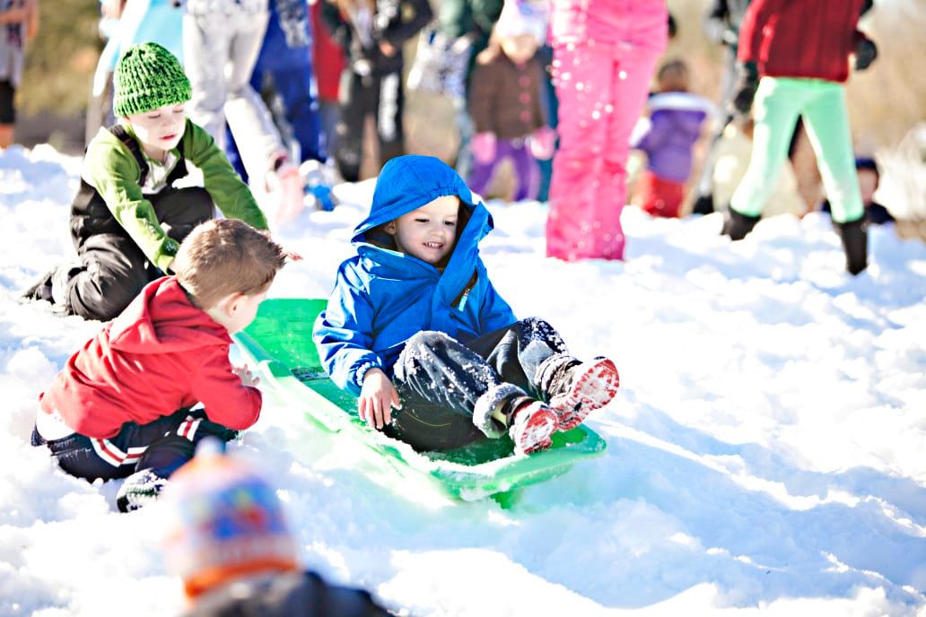 boys sledding in crowded park in bright sunshine and snow