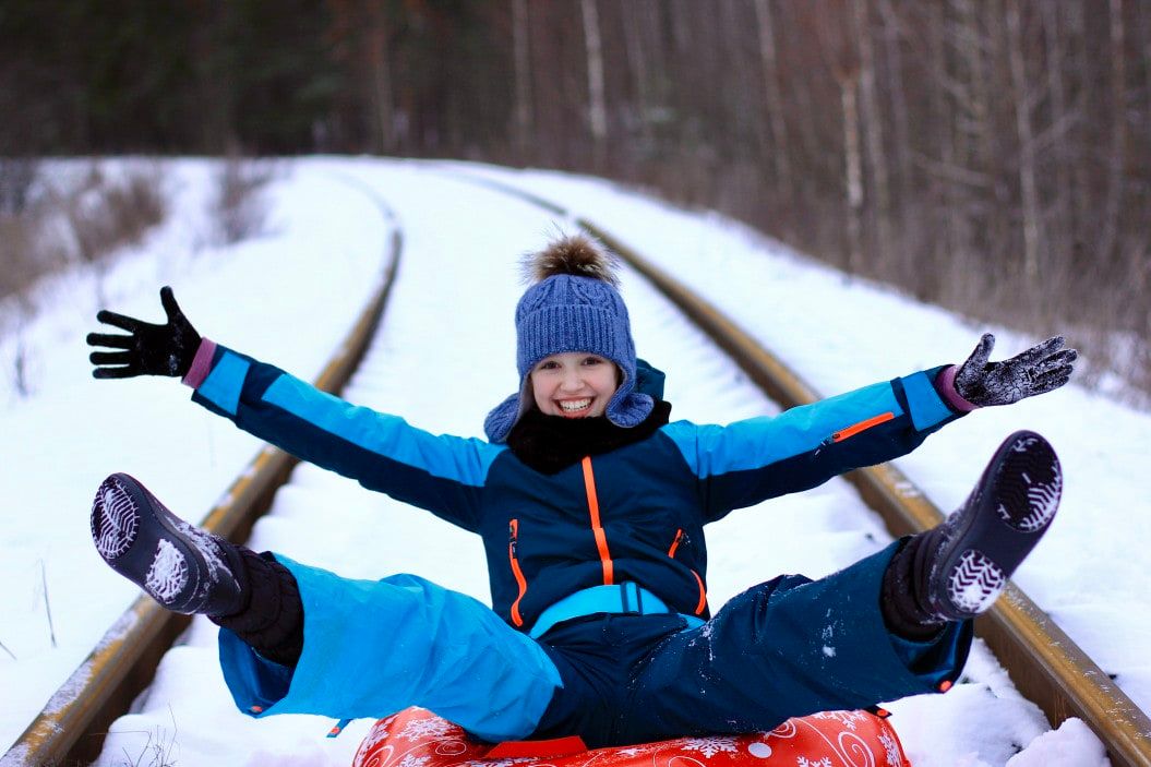 girl in snowsuit sledding down tracks in winter