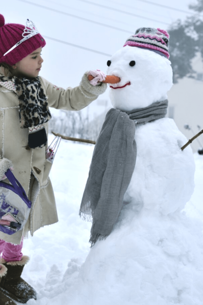 girl building a snowman outdoors winter
