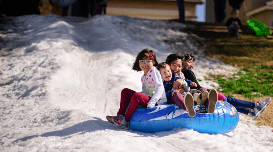 kids snow tubing ouside in melting snow on blue tube