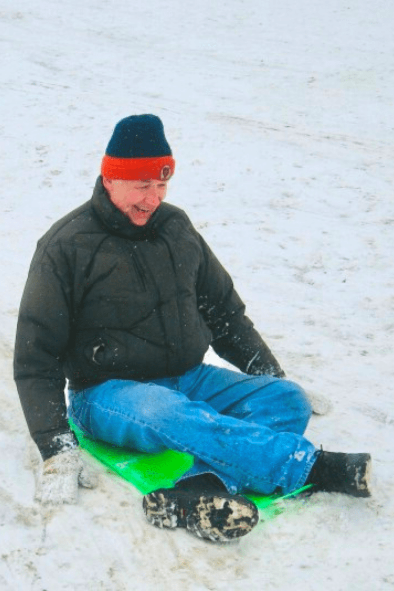 older man sledding on hill on flexible plastic toboggan