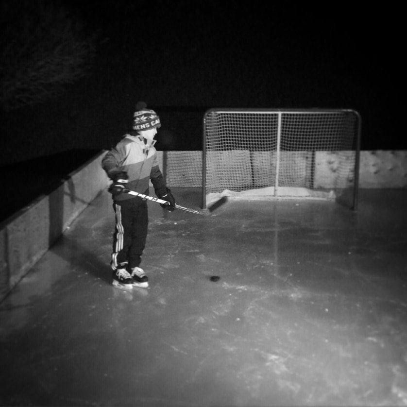 black and white night shot boy playing hockey in backyard ice rink