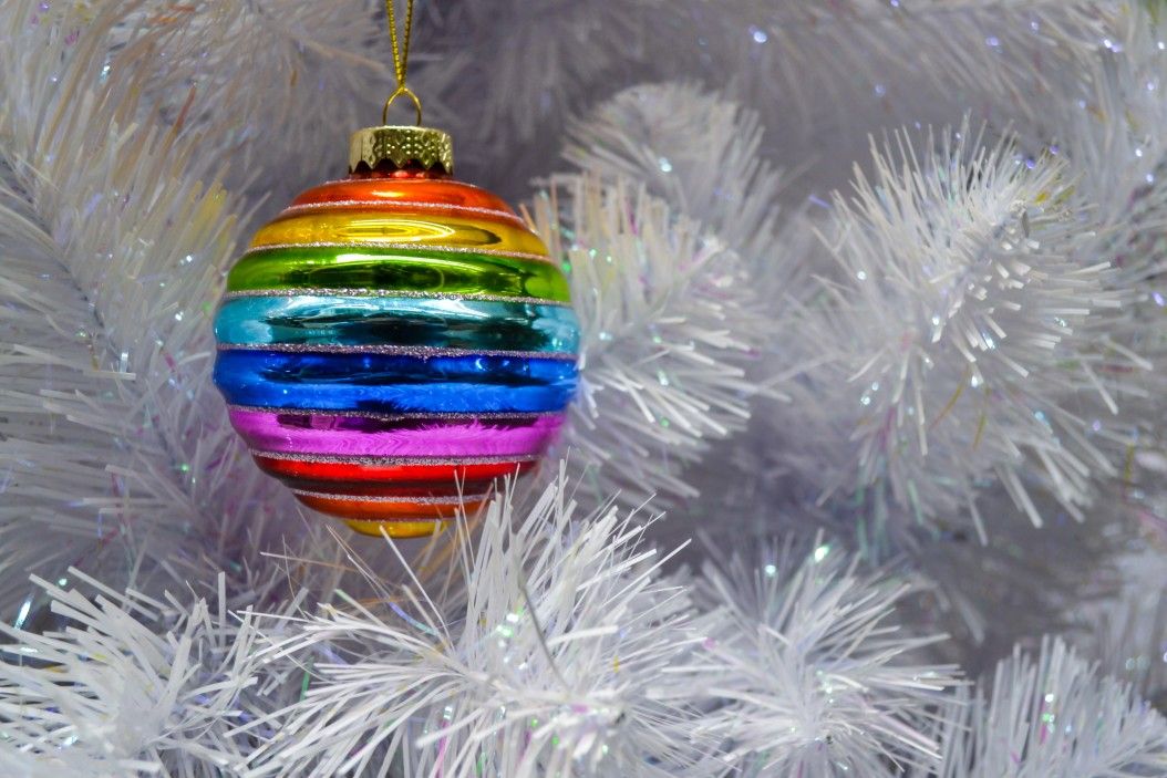 Bright glass rainbow colored Christmas ball, bauble hanging on a white artificial christmas tree