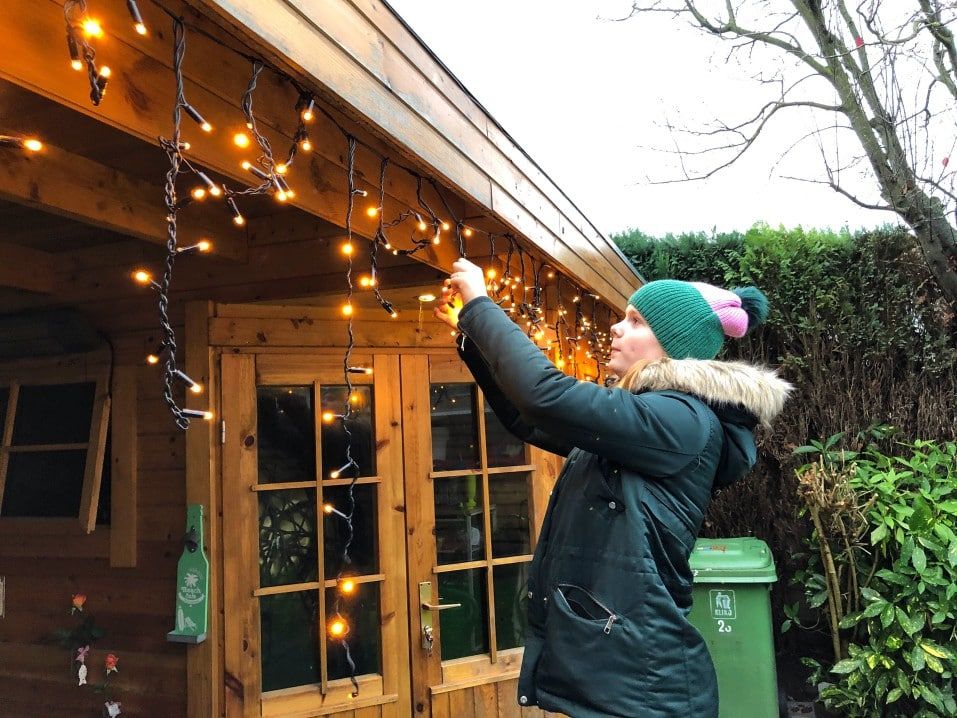 woman hanging christmas lights on home exterior