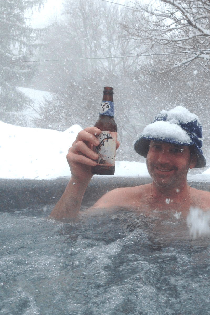 hot tub winter guide tall man in hot tub snowfall winter hat holding beer