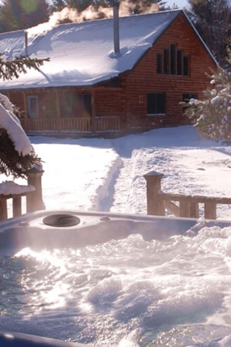 a well maintained hot tub running in winter near a cabin with snow