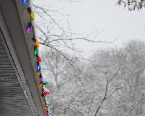 Old fashioned Christmas lights hang from the roof of the house on a snow day