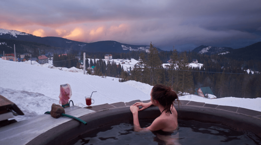 a woman in a hot tub outdoors in winter overlooking mountain view