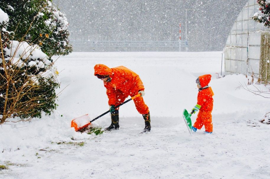 Man and small child clearing snow with shovels in winter