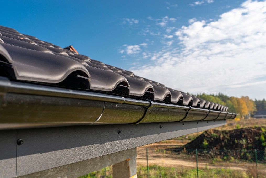 A metal, black gutter on a roof covered with ceramic tiles. Close up shot. roof gutter