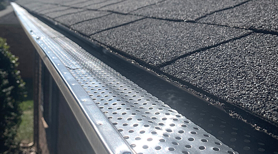 a gutter with gutter guards installed on a shingled roof closeup