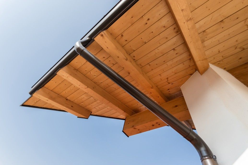 New wooden warm ecological house roof with steel gutter rain system. Professional construction and drainage pipes installation. Eco materials.