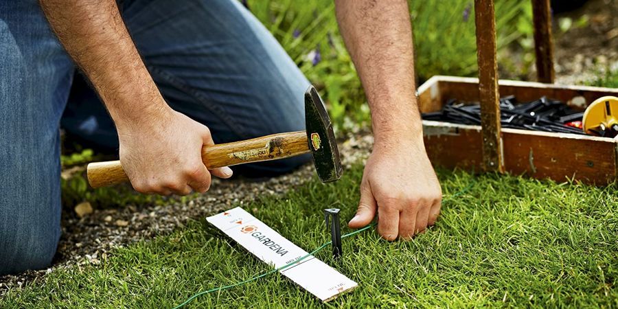 A man hammers a guidewire peg for robotic mowing navigation into the lawn.