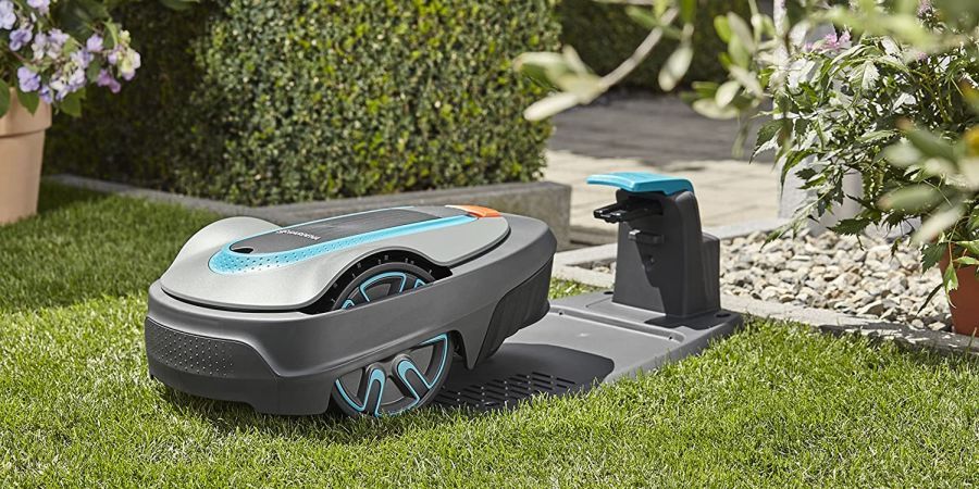 A two-tone grey robotic mower approaches its charging station.