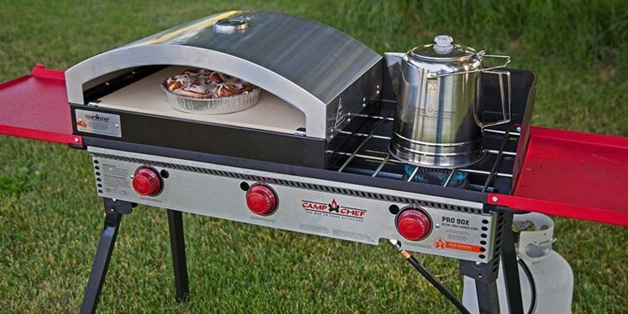 A shiny stainless steel and red outdoor pizza oven with ample cooking space, including oven, burner, and foldout tables.