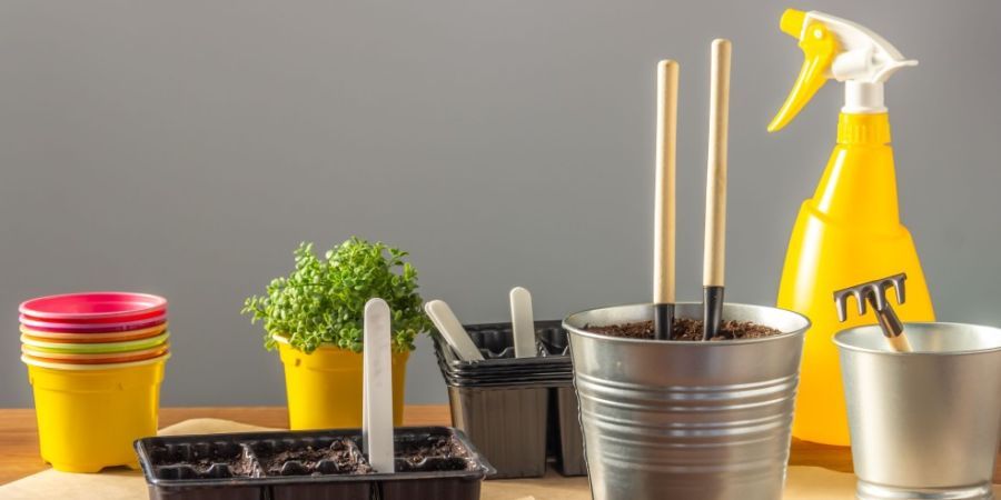 Seedling container filled with earth, small shovels and a rake for plant care, colorful plastic pots.