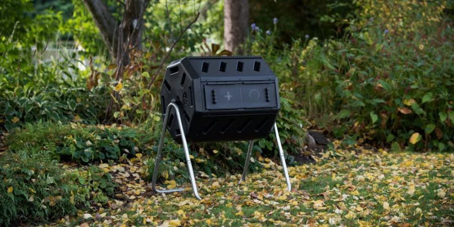 Dual chamber tumbling composter standing on lawn covered in yellow fallen leaves.