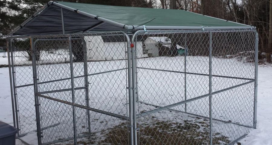 Winter-proofed outdoor dog kennel standing on snow-covered lawn.