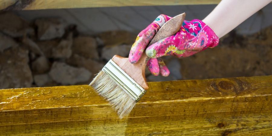 Woman wearing glove holding a brush as she's staining a beam.