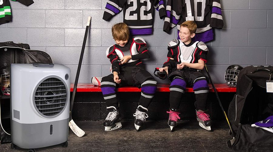 Two kids in ice hockey gear sitting on a red bench in an ice hockey change room with an evaporative cooler next to them.