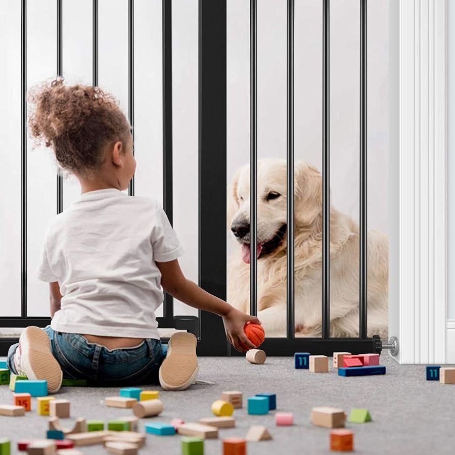 A child sits on one side of a baby gate playing with blocks and a dog sits on the other.