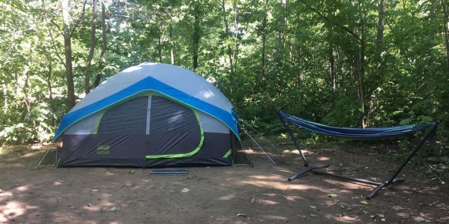 A grey, blue and lime green dome tent set up outdoors next to a powder-coated steel hammock stand holding a blue striped hammock