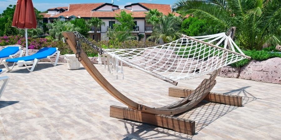 a wooden hammock stand on a stone tile patio area, holding a white rope hammock
