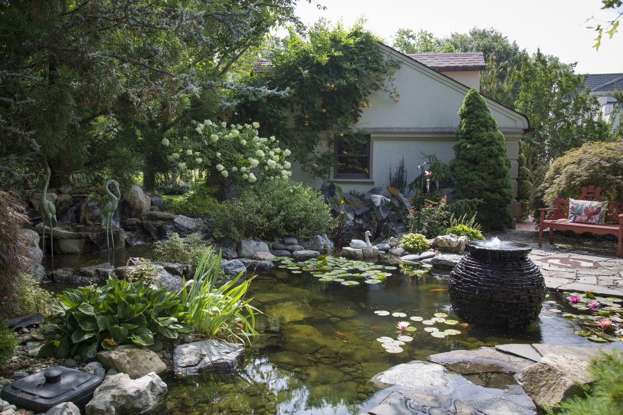koi pond at edge of patio with fountain, waterfall, statues, and plants