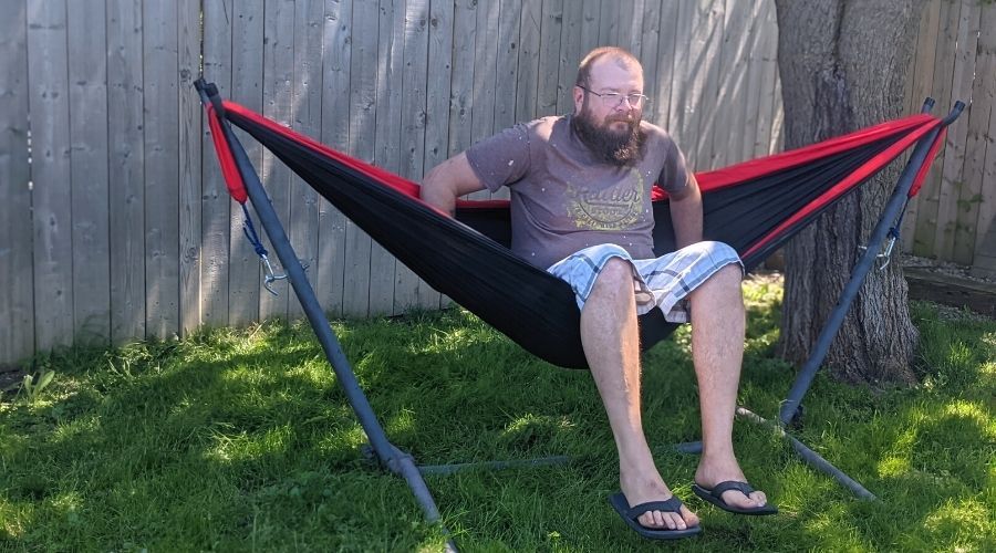 A man getting into a red and black hammock.