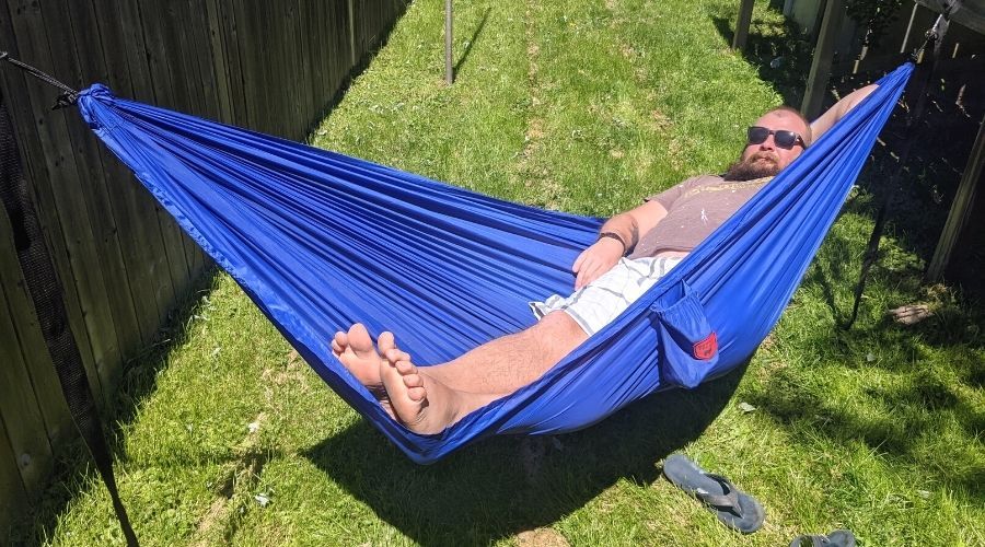 a man stretched out and sleeping in a blue parachute hammock