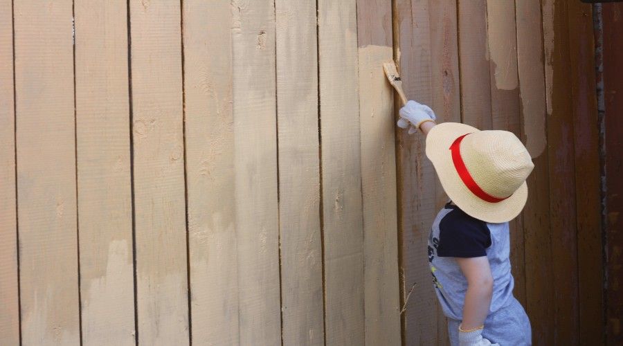 A child painting a fence wearing a straw sun hat