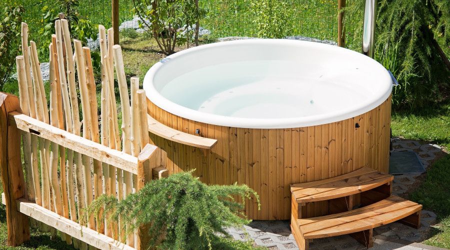 Wooden hot tub with greenery in background and rustic privacy fence