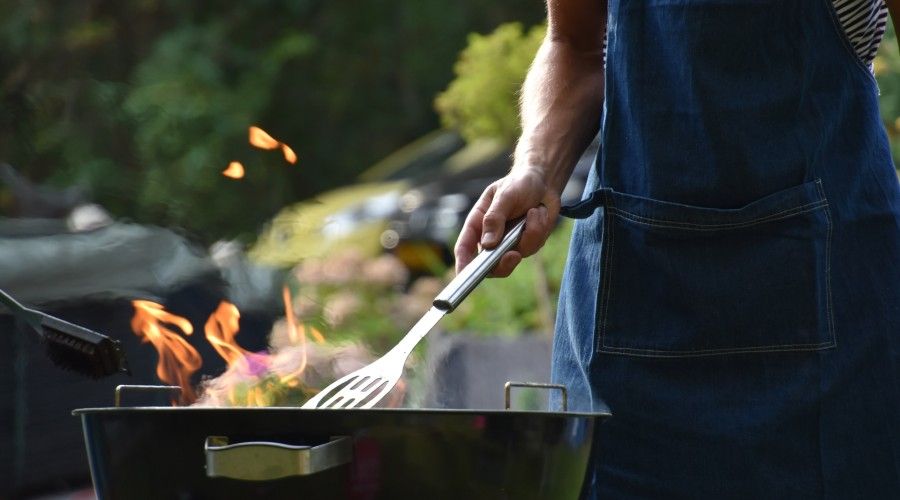 A person holding a grilling spatula over a grill with flames