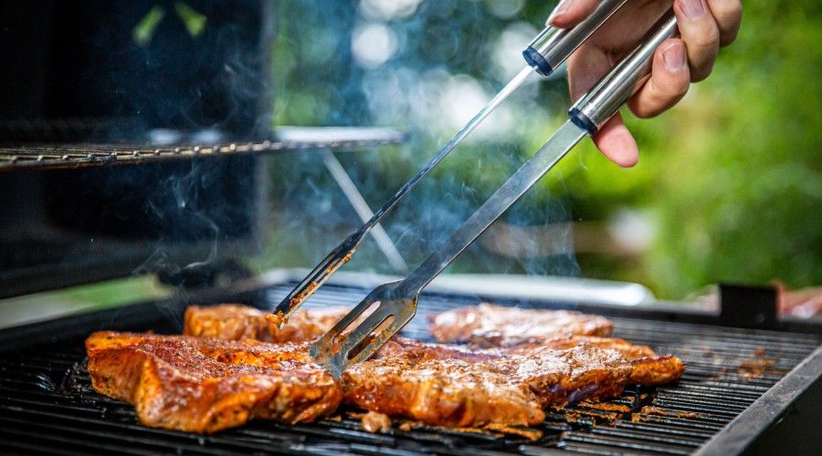 A person's hand reaching out to flip steak on a bbq