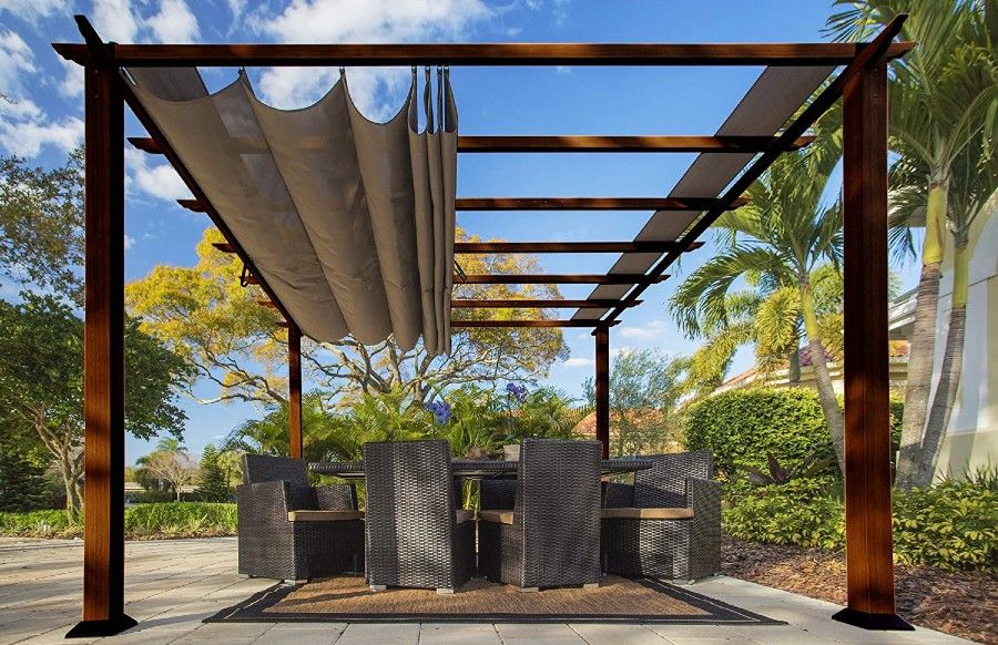 A pergola with a canopy set up with a table and wicker chairs beneath it