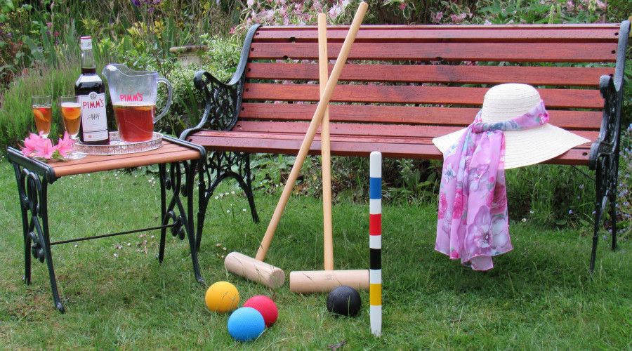 croquet set leaning against garden bench with tea on table and jacket draped on bench