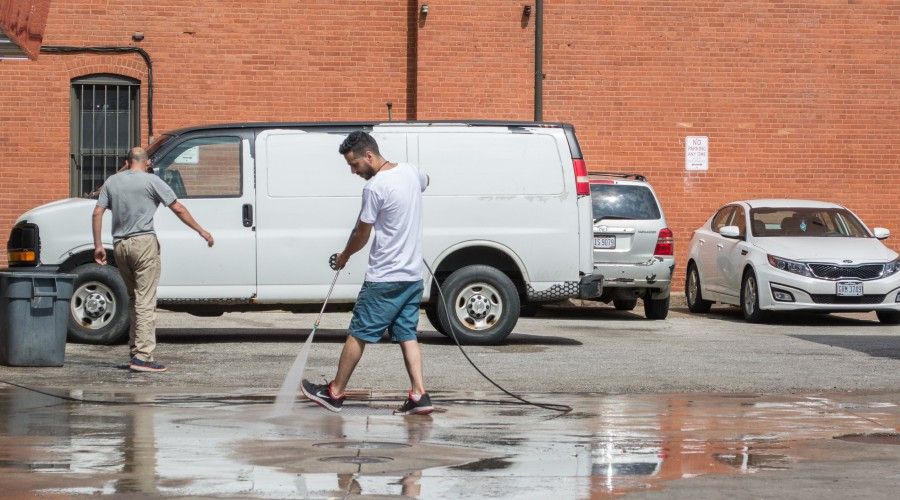 A man wearing a white tshirt and blue shorts power washing a parking lot space