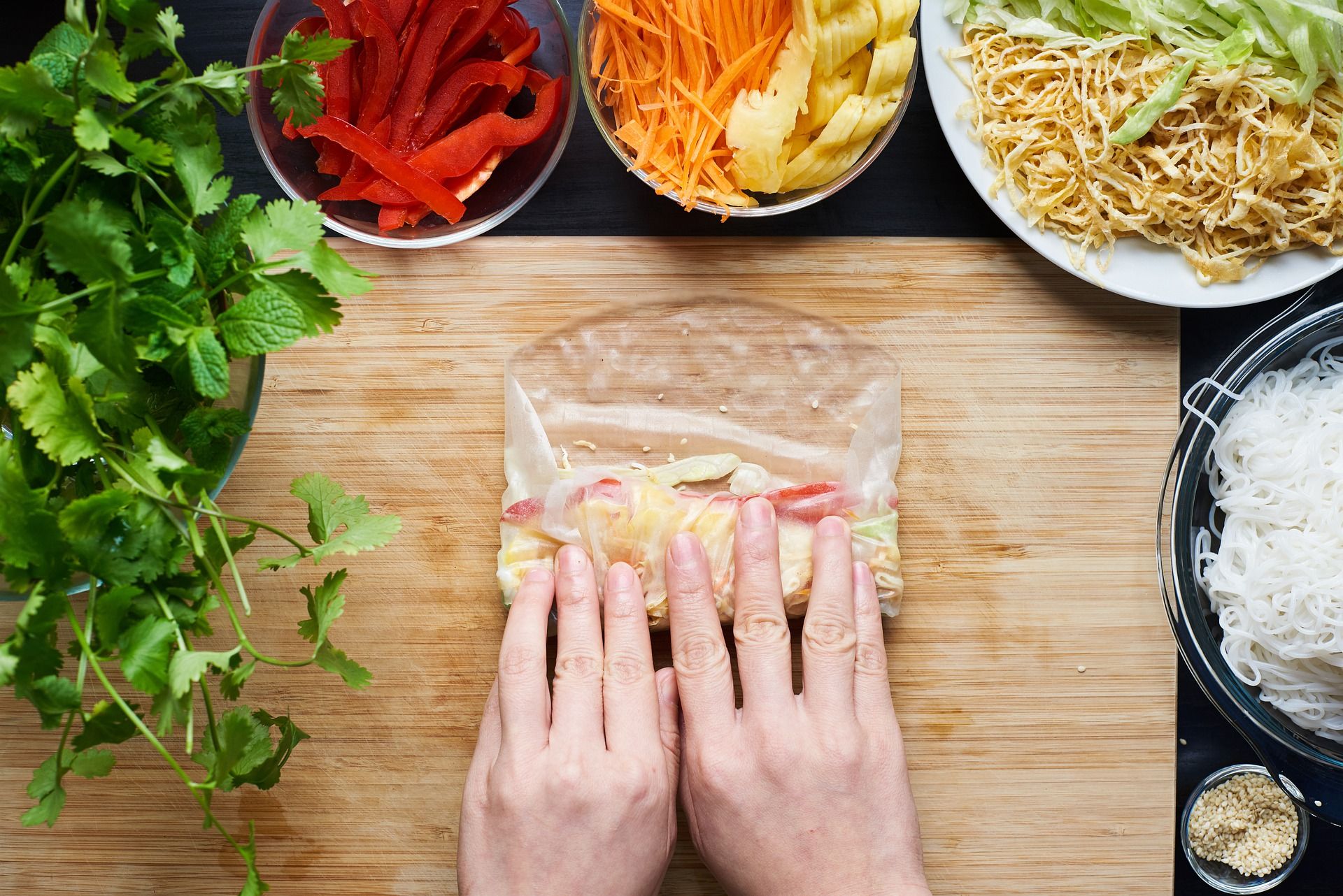 A person rolling a spring roll with vegetables