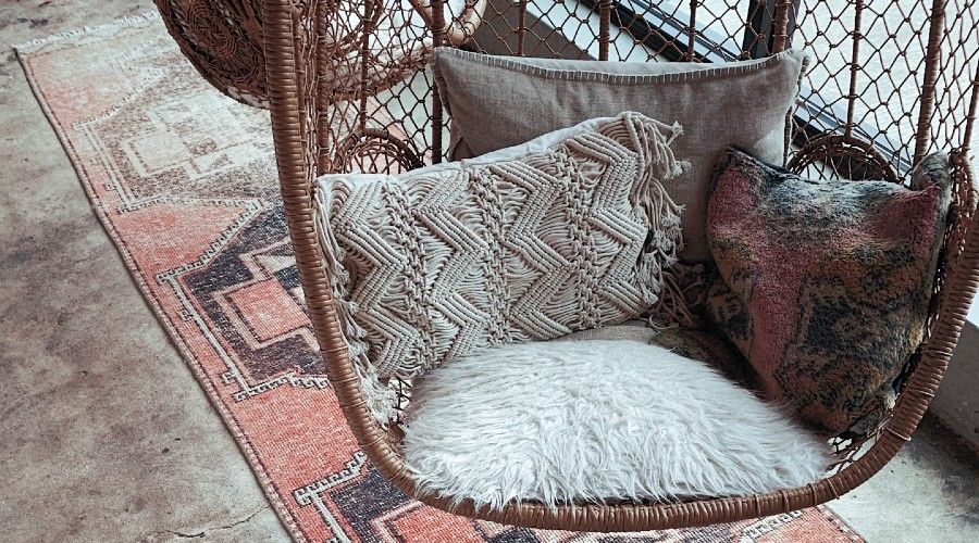 four different grey pillows sitting in a hanging wicker chair
