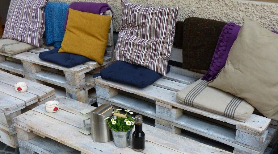 an assortment of different colored throw pillows on a bench made from pallets