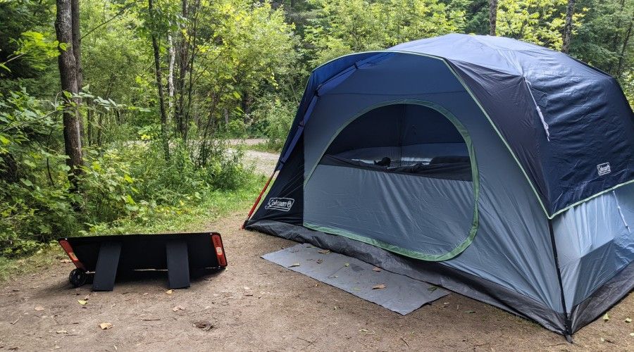 A camping tent sitting outside with a solar panel set up on the ground in front of it