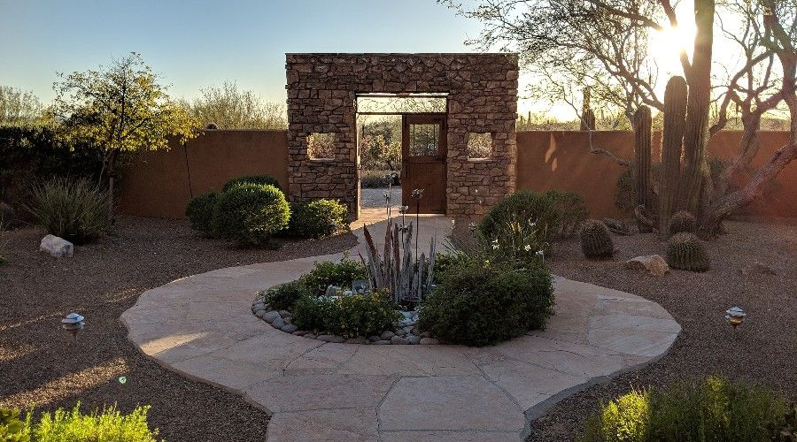 Xeriscaped area with patio pavers and squared arch doorway at end of path