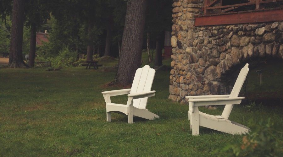 two Adirondack chairs sitting in the front yard by a stone house