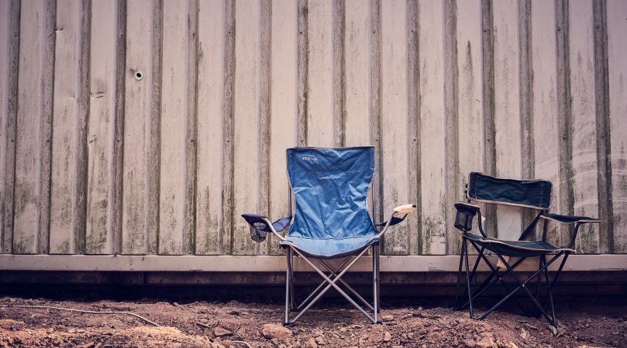two camping foldup chairs sitting against a wall outdoors