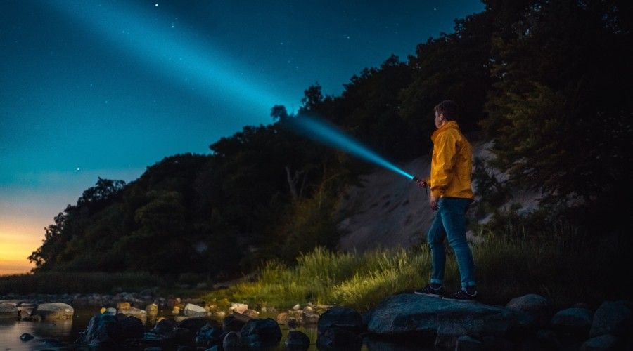 man holding flashlight standing on gray stone during nighttime