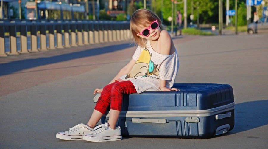 young girl sitting on a suitcase outside