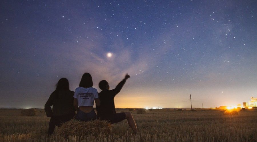 three people sitting outdoors looking at stars