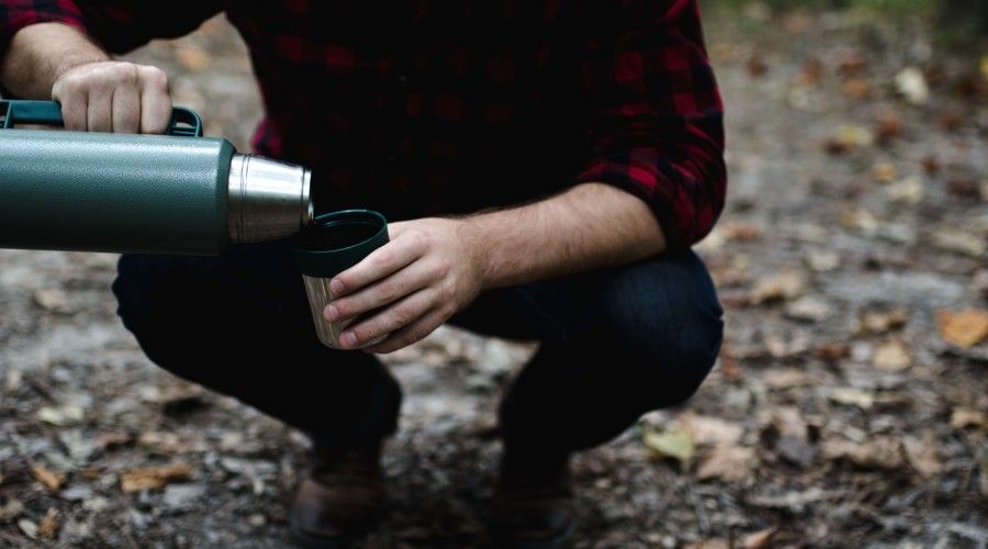 man bending his knees pouring thermos contents in cup
