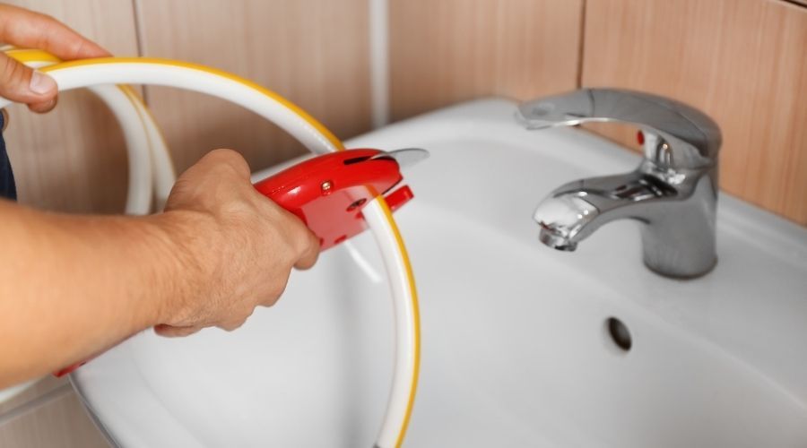 a person cutting a yellow and white hose over a sink